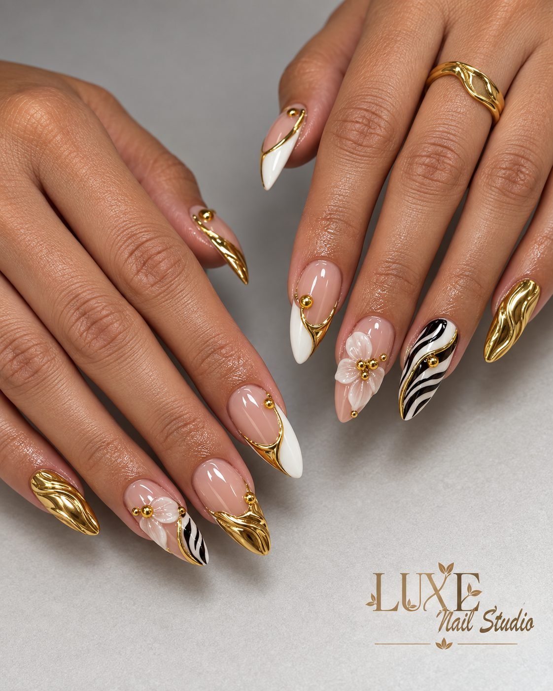 Nude almond nails with gold chrome, a white flower, and zebra tips by Luxe Nail Studio