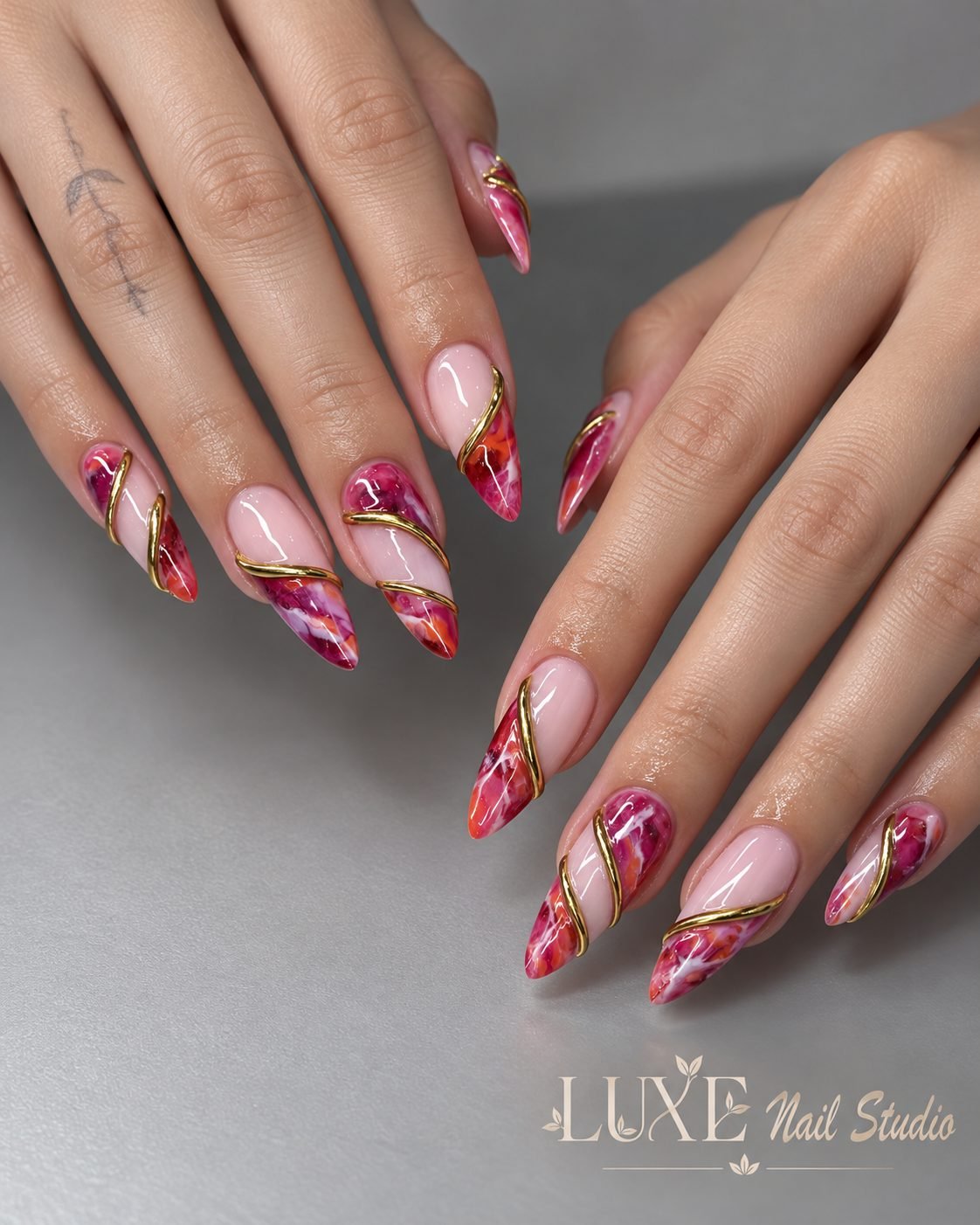 Pink almond nails with magenta marble tips and raised gold swirls by Luxe Nail Studio